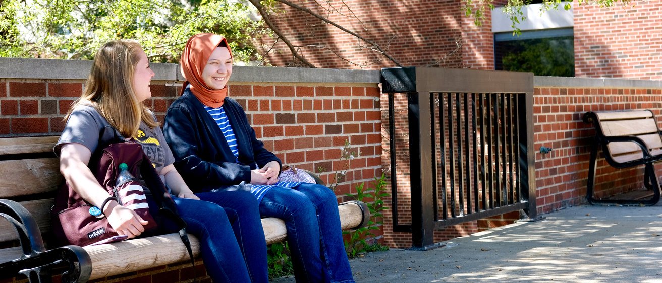 International Studies students laughing together on a campus bench.
