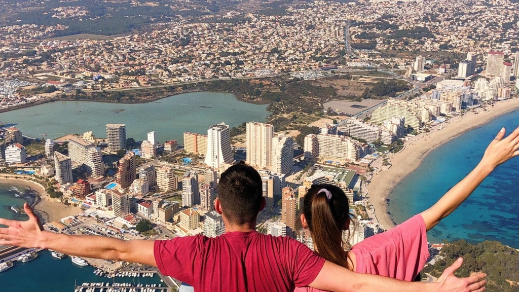 two people stand high above a sprawling city with arms outstretched